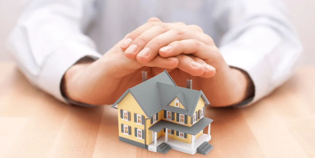Hands protecting a small model house symbolizing home insurance and property security