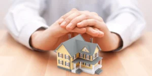 Hands protecting a small model house symbolizing home insurance and property security